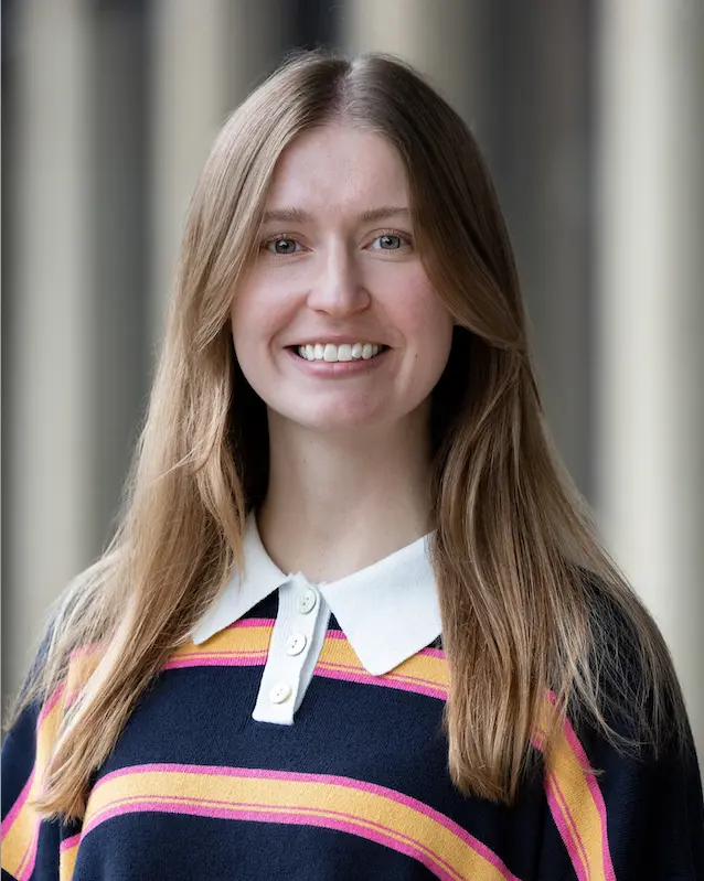 Woman smiling with a while collared and navy, yellow, and pink striped sweater.