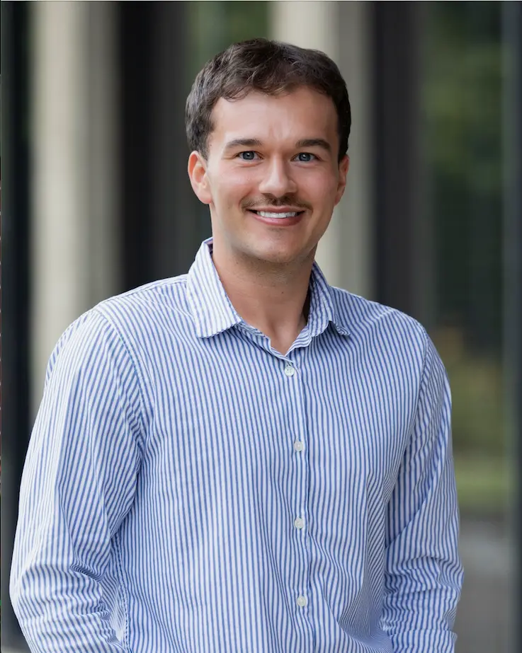Man smiling with a blue and white striped button down shirt.