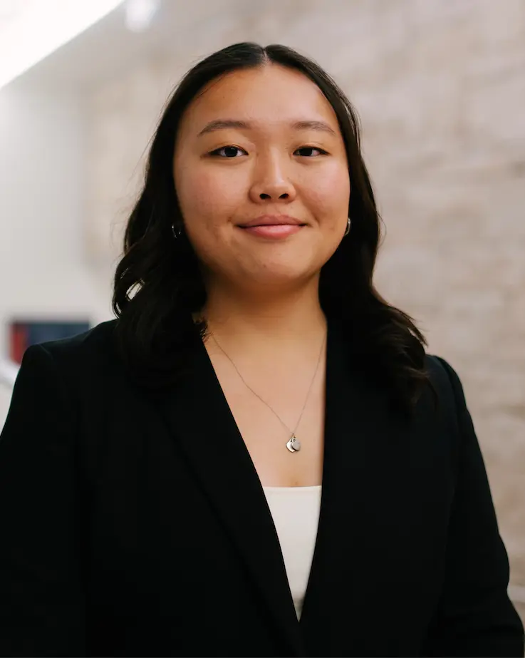 Woman smiling with a black blazer and silver heart shaped necklace.